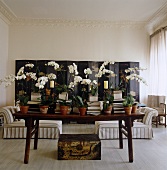 Orchids are interspersed with piles of books on the table in this living room while a large Chinese folding screen decorates the back wall