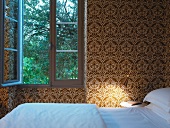 Schlafzimmer mit gold weissem Ornamentmuster auf Tapete an Wand und göffnetem Fenster