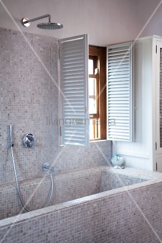 Badewanne und Wand mit hellen Mosaikfliesen und offene Innenläden am