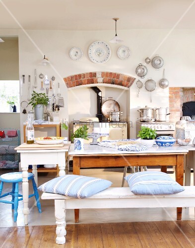 Weisse Bank mit Sitzkissen und rustikale Tische vor Küchenherd in