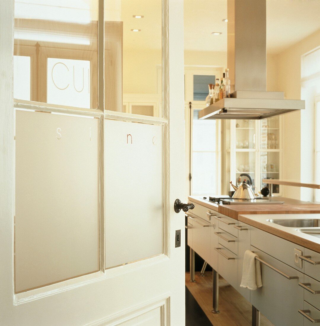 Blick durch eine offene Tür in einer Küche mit Edelstahl-Dunstabzugshaube über Kochinsel