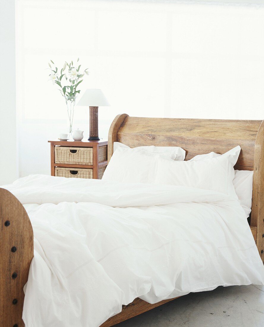 Ein rustikales Doppelbett mit weißem Bettbezug im hellen Schlafzimmer