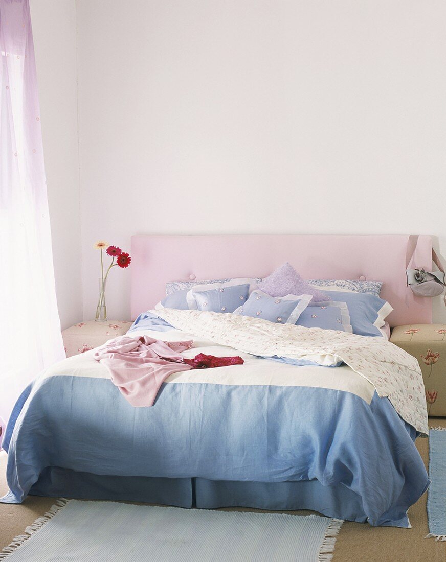 Ein Doppelbett mit blau-weißen Bettbezug und rosa Kopfteil