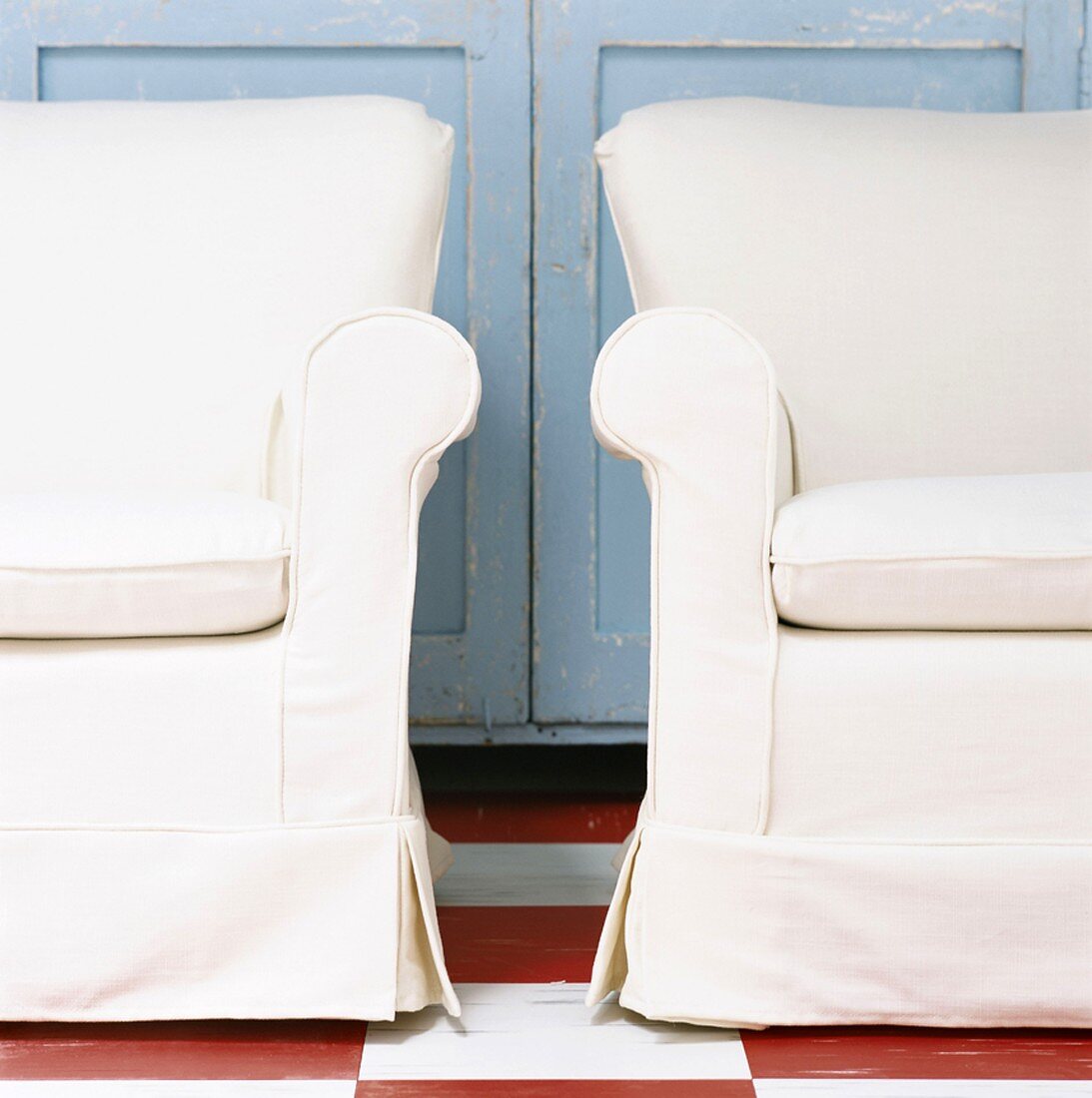 Ausschnitt zweier Sessel mit weißem Bezug vor blau lackierte Holzschranktüren