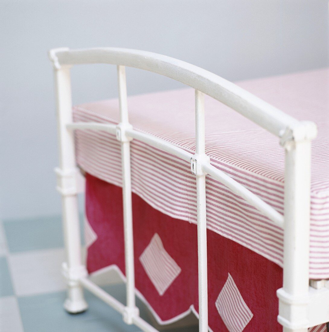 Fußende eines schmiedeeisernes Einzelbett mit rosa-weiß gestreiften Bettbezug