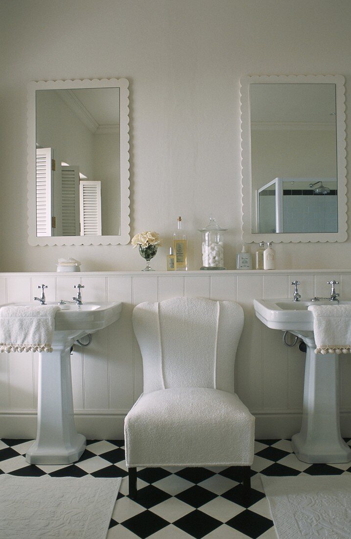 Weißer Sessel zwischen zwei Waschbecken im Badezimmer mit Bodenfliesen im Schachbrettmuster