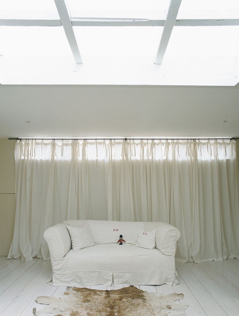 weiße Couch und Tierfell unter Deckenöffnung im schlichten Wohnbereich mit Dielenboden