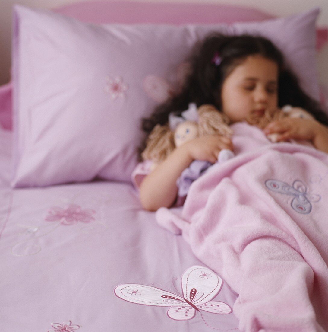 Mädchen schläft im Bett und hält eine Puppe