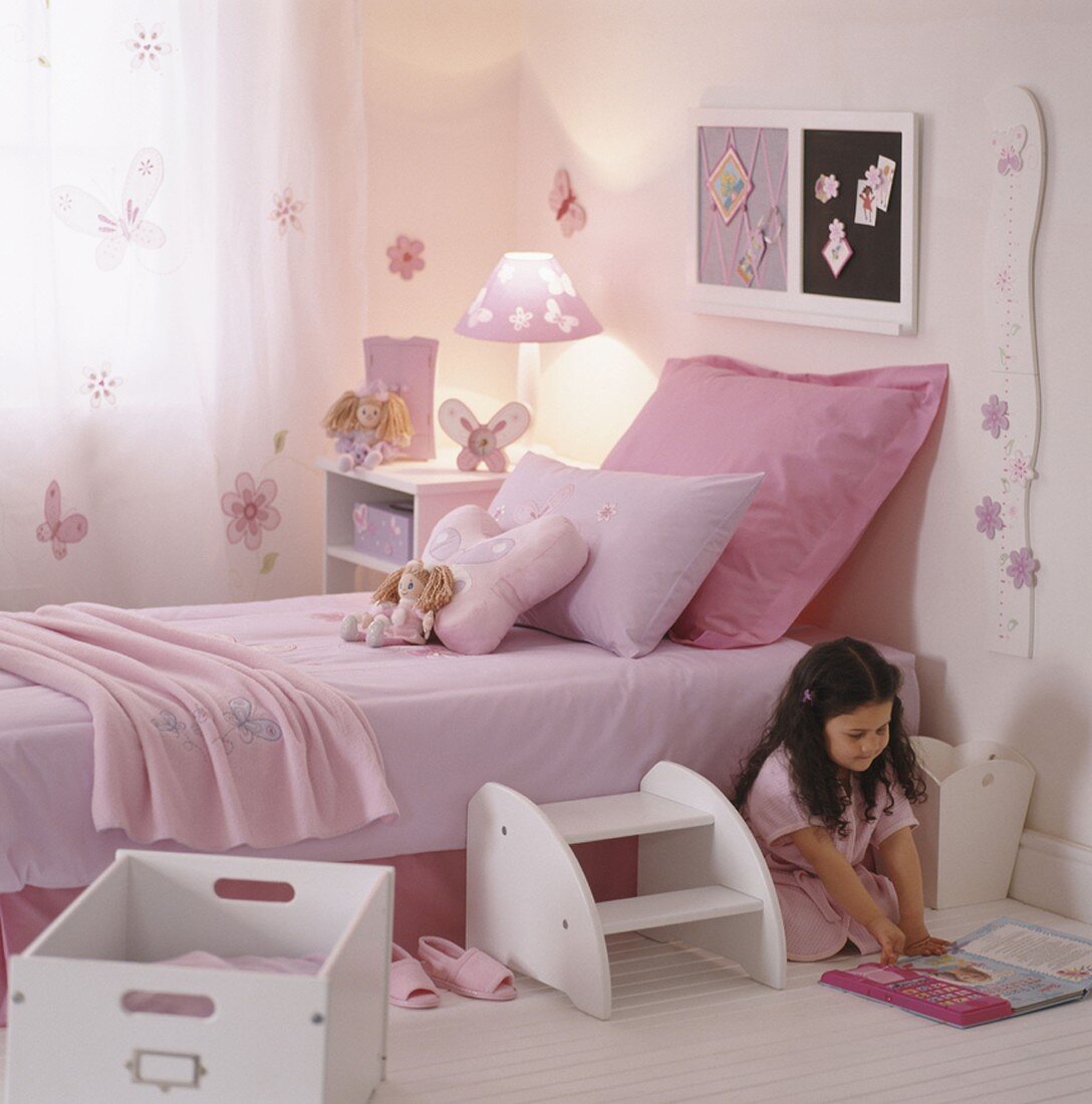Mädchen liest ein Buch neben dem Bett in ihr rosa Kinderzimmer