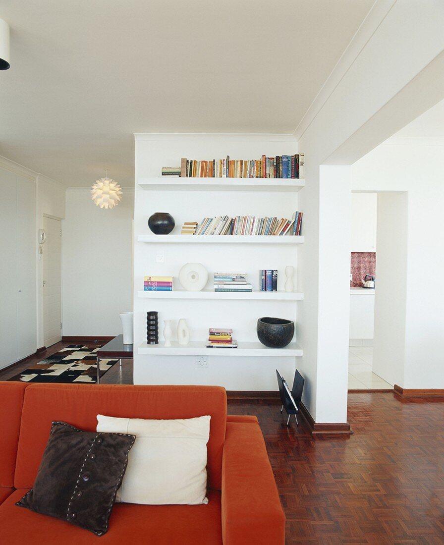 Blick auf ein Bücherregal hinter einer roten Couch