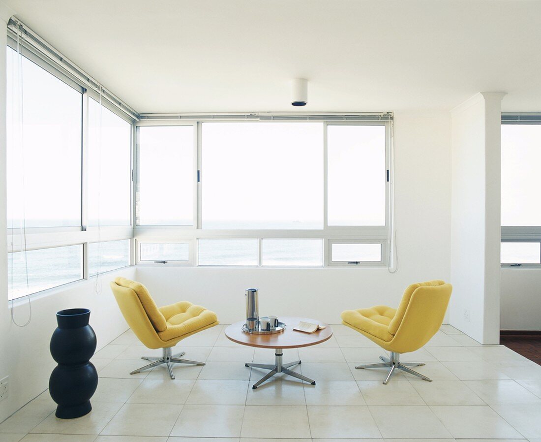 Zwei gelbe Sessel und ein runder Tisch im offenen Raum mit Eckfenster und Meeresblick