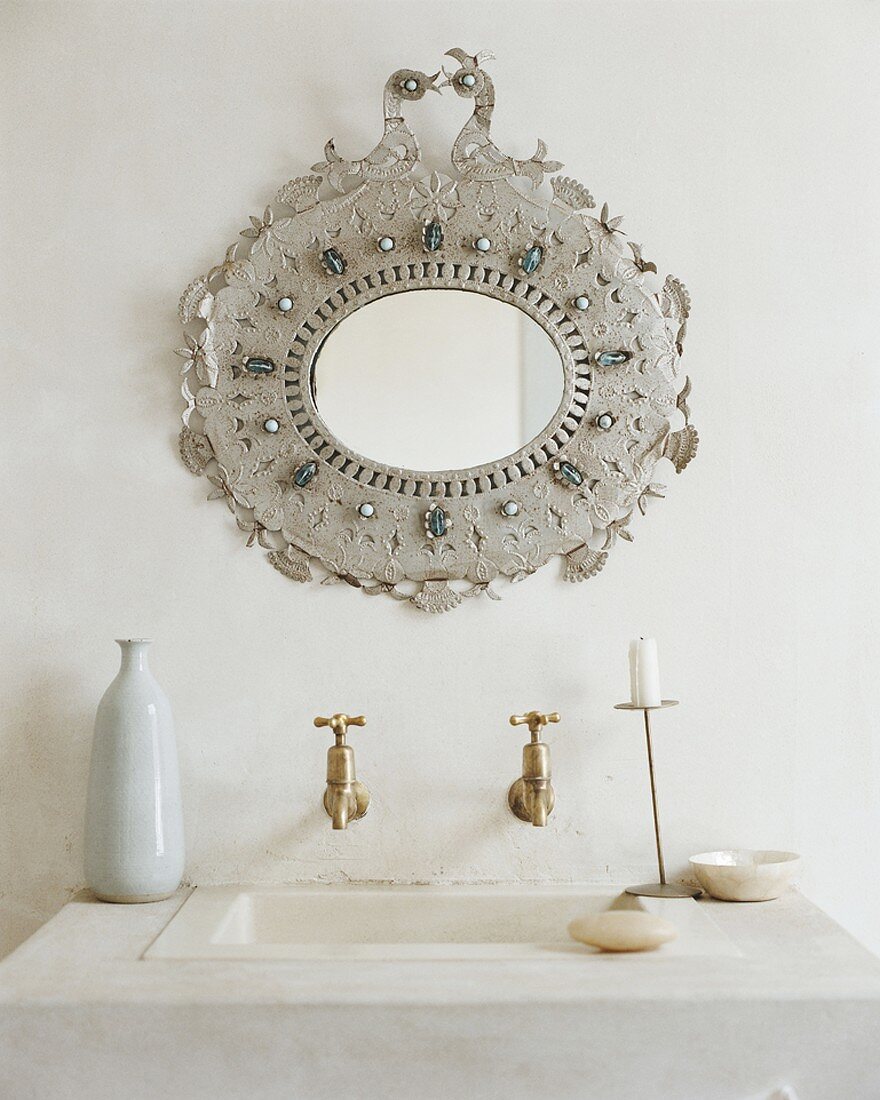 Ein Waschbecken mit alten Bronzewasserhähne unter reich verzierter Wandspiegel
