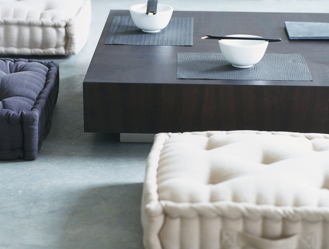 Sitzkissen vor einem niedrigen Tisch mit weißen Schalen im asiatischen Stil