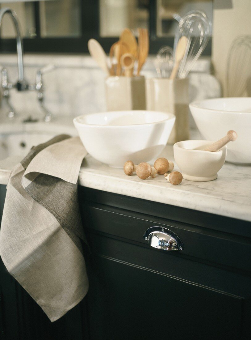 Porcelain bowls and a porcelain mortar with a wooden pestle on a light marble kitchen counter next to fresh mushrooms