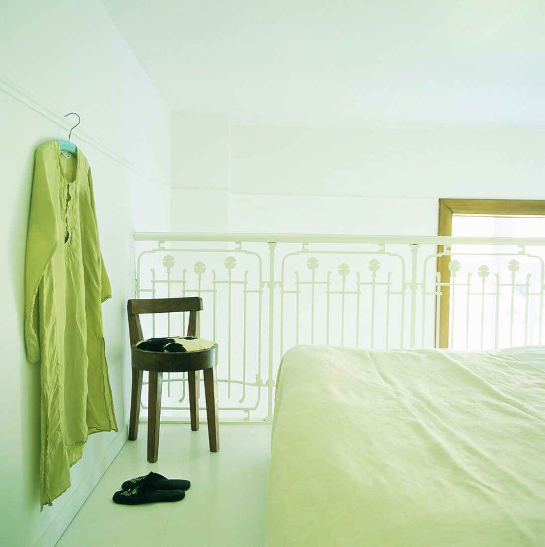 Doppelbett auf Galerie mit weißem Geländer; an der Wand hängt ein Kleidungsstück am Kleiderbügel