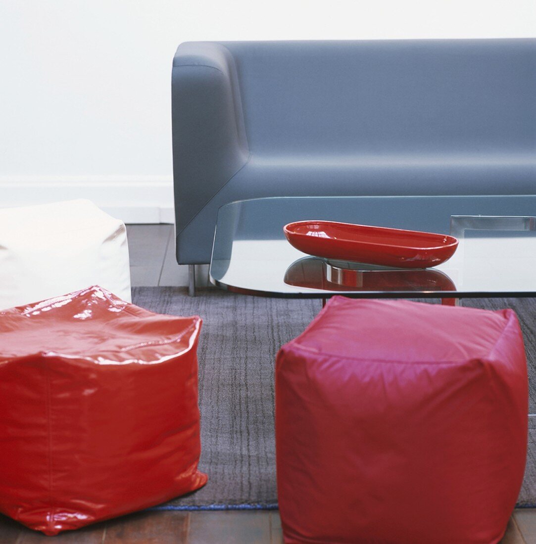 Rote Sitzhocker, blaue Couch und Glastisch mit roter Schale im Wohnzimmer