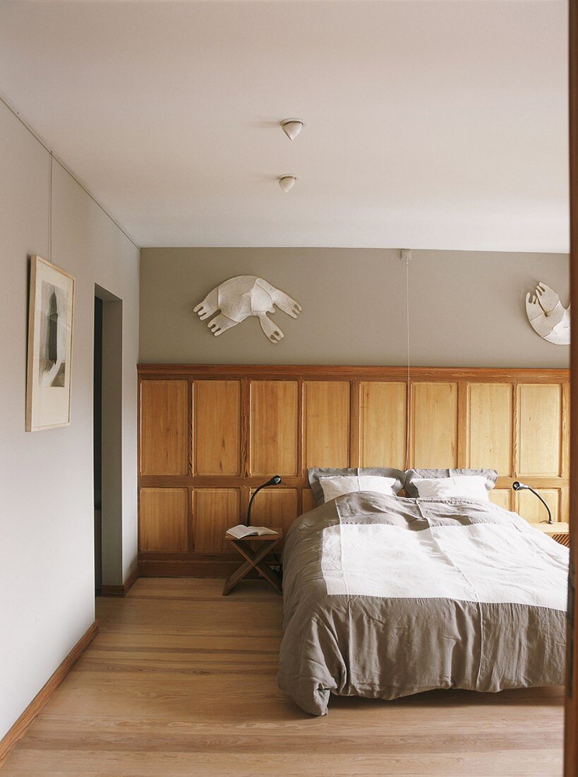 Schlafzimmer mit Doppelbett, einer Wandverkleidung aus Holz und darüberhängenden Kunstobjekten