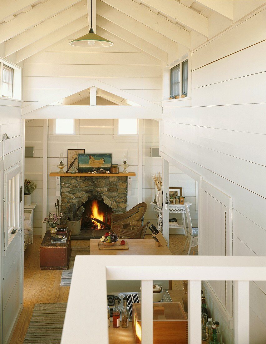 View from gallery down into open-plan interior of wooden house with fire in open fireplace