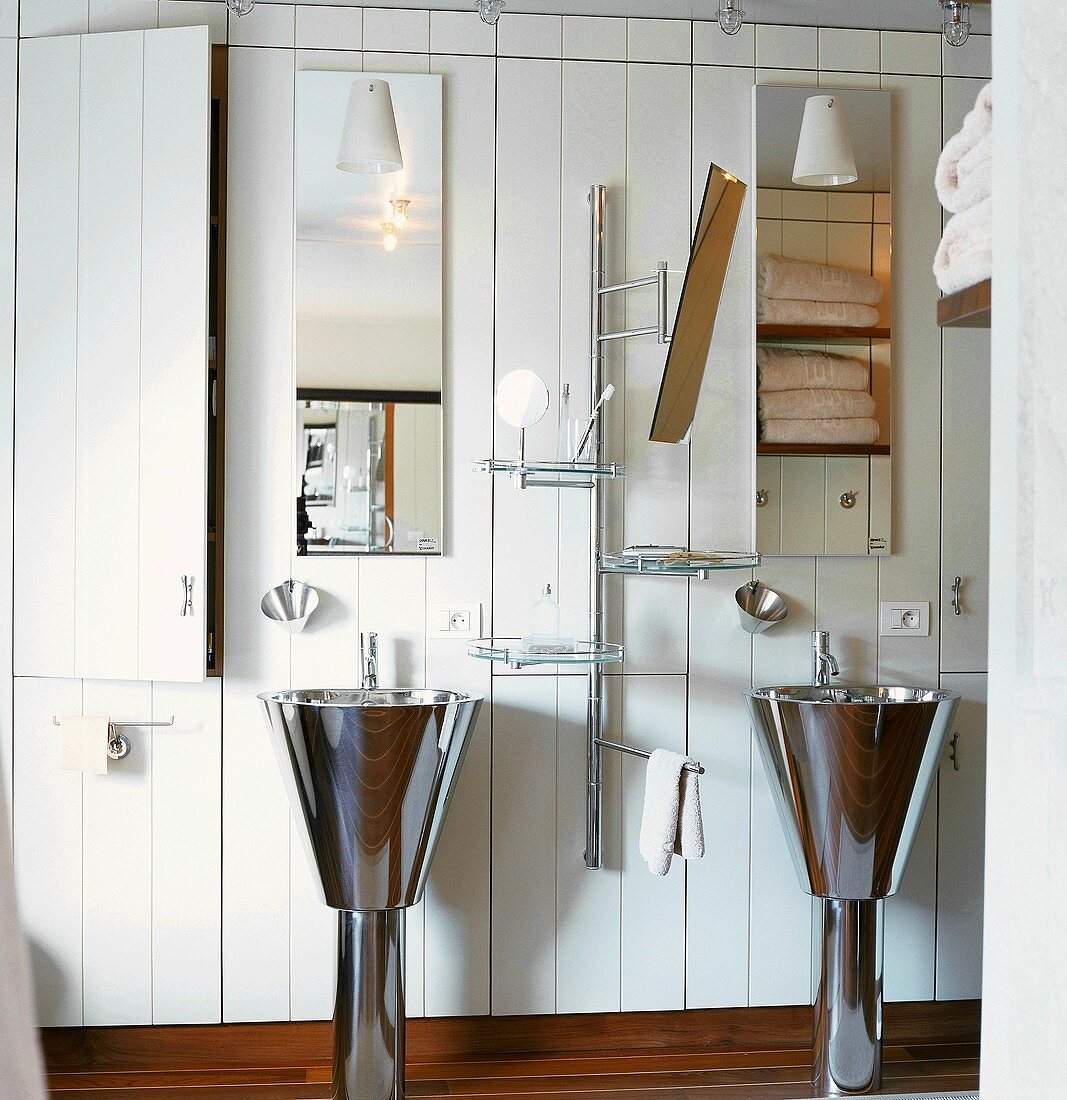 Twin stainless steel, pedestal washbasins in bathroom with white wooden wall