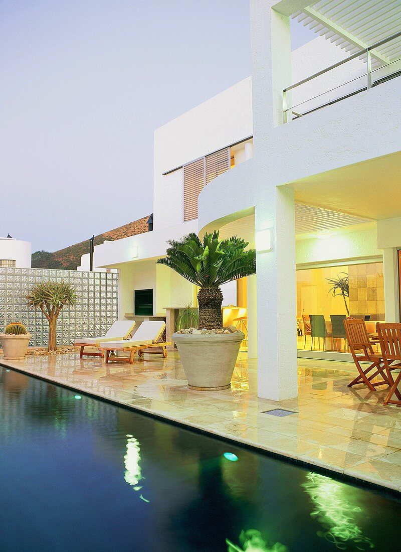 Liegestühle und exotische Pflanzen auf der Terrasse eines Hauses mit Swimmingpool