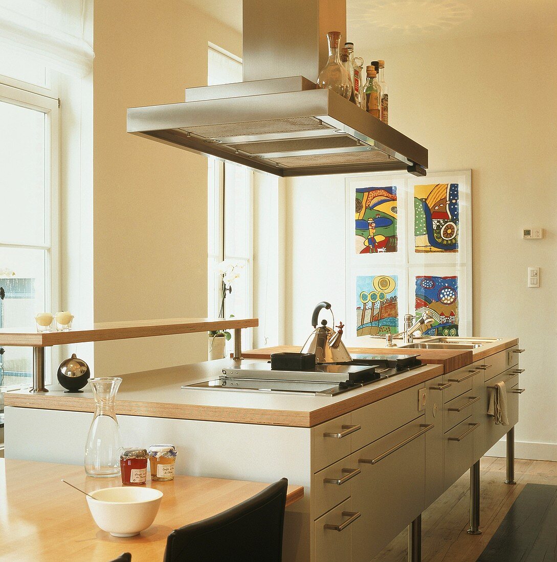 Island counter with integrated hob and sink, metal handles and extractor hood used as shelf for bottles