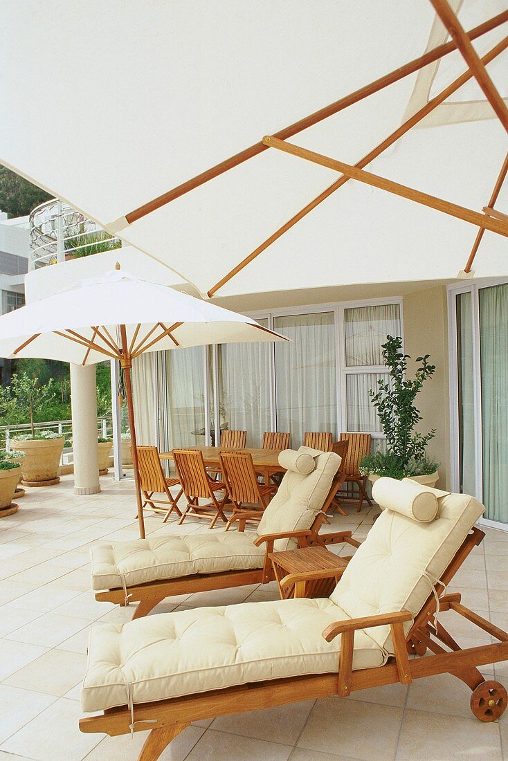 Sonnenterrasse mit weissen, quadratischen Sonnenschirmen, Holzliegestühlen und einem Esstisch mit Klappstühlen