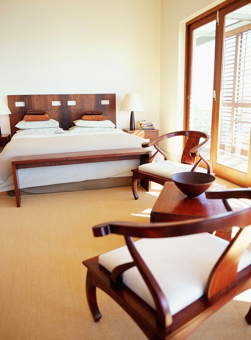 Modernes Schlafzimmer mit Doppelett, Bank und bequemen Stühlen aus Edelholz