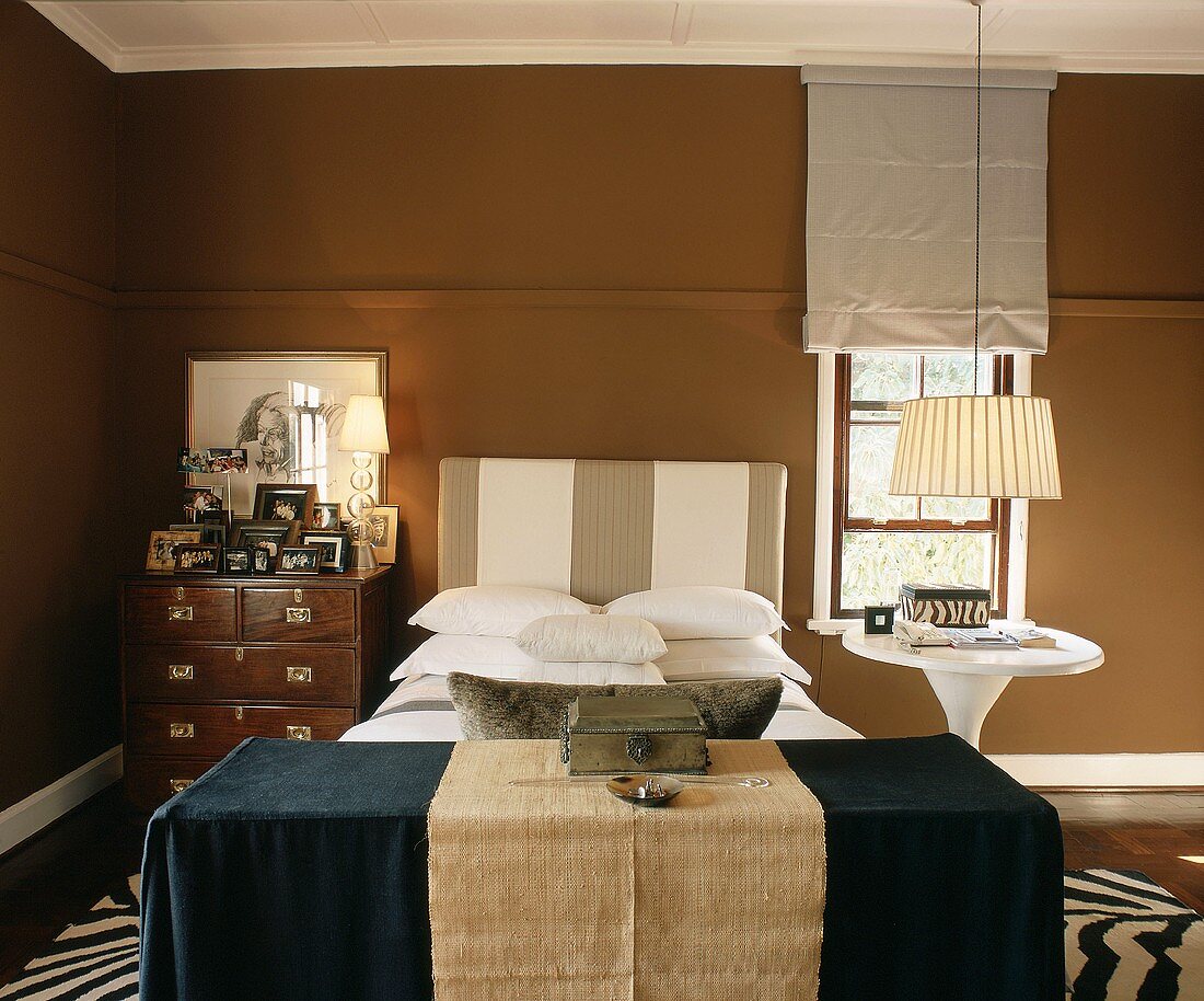 Bedroom in shades of brown with striped headboard and antique chest of drawers