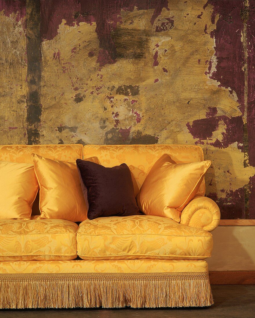 Goldenglänzende Couch mit Kissen und Fransen vor großem, modernen Gemälde mit Holzrahmen