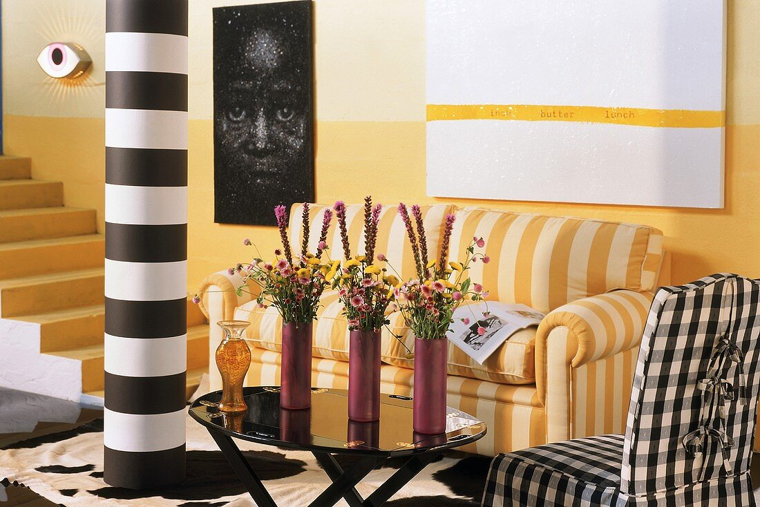 Lebendiger Raum mit gelbem Treppenaufgang, gestreifter Couch im selben Farbton und schwarz-weissen Kontrapunkten