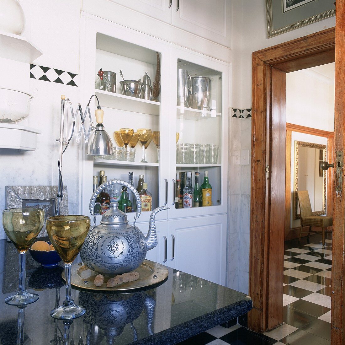 Küche mit großem, eingebauten Vitrinenschrank und mit Blick auf den glänzenden Esszimmerboden in schwarz-weißem Schachbrettmuster