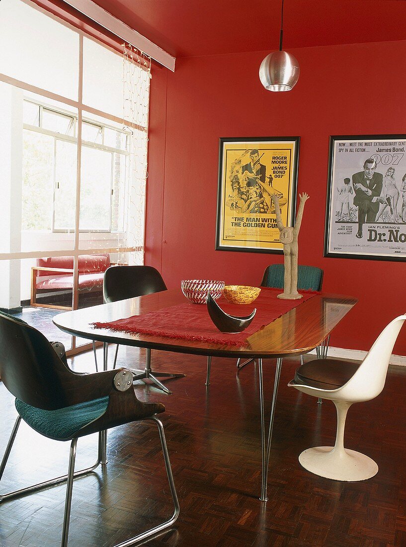 Dining table, designer chairs and framed film posters in red room with glass wall