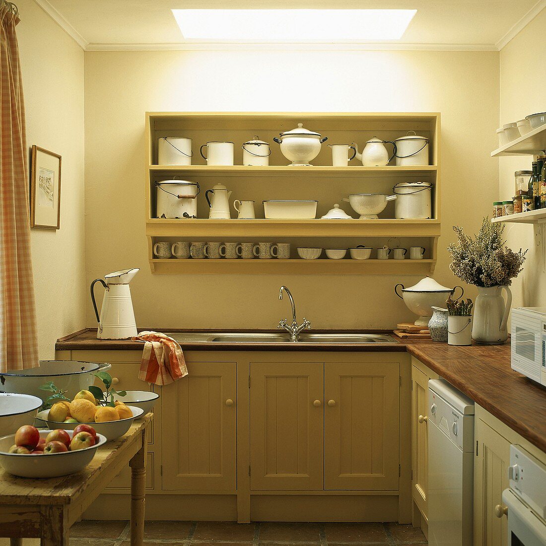 Simple kitchen with wooden cabinets and collection of enamel crockery on wall-mounted shelves