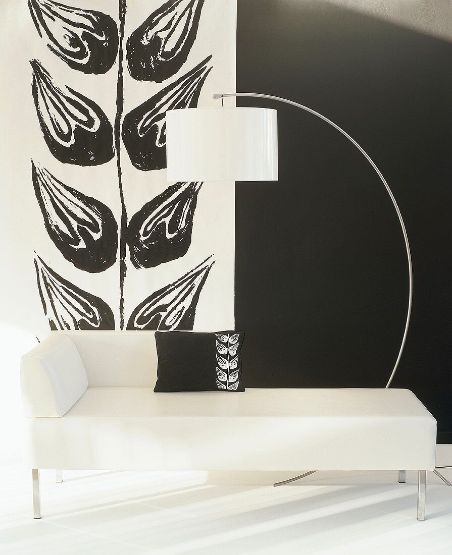 Schwarz-weiße Raumecke mit weisser Recamiere mit Kissen mit Blattmotiv, weisser Bogenlampe und einem sich wiederholenden Blattmotiv an der Wand