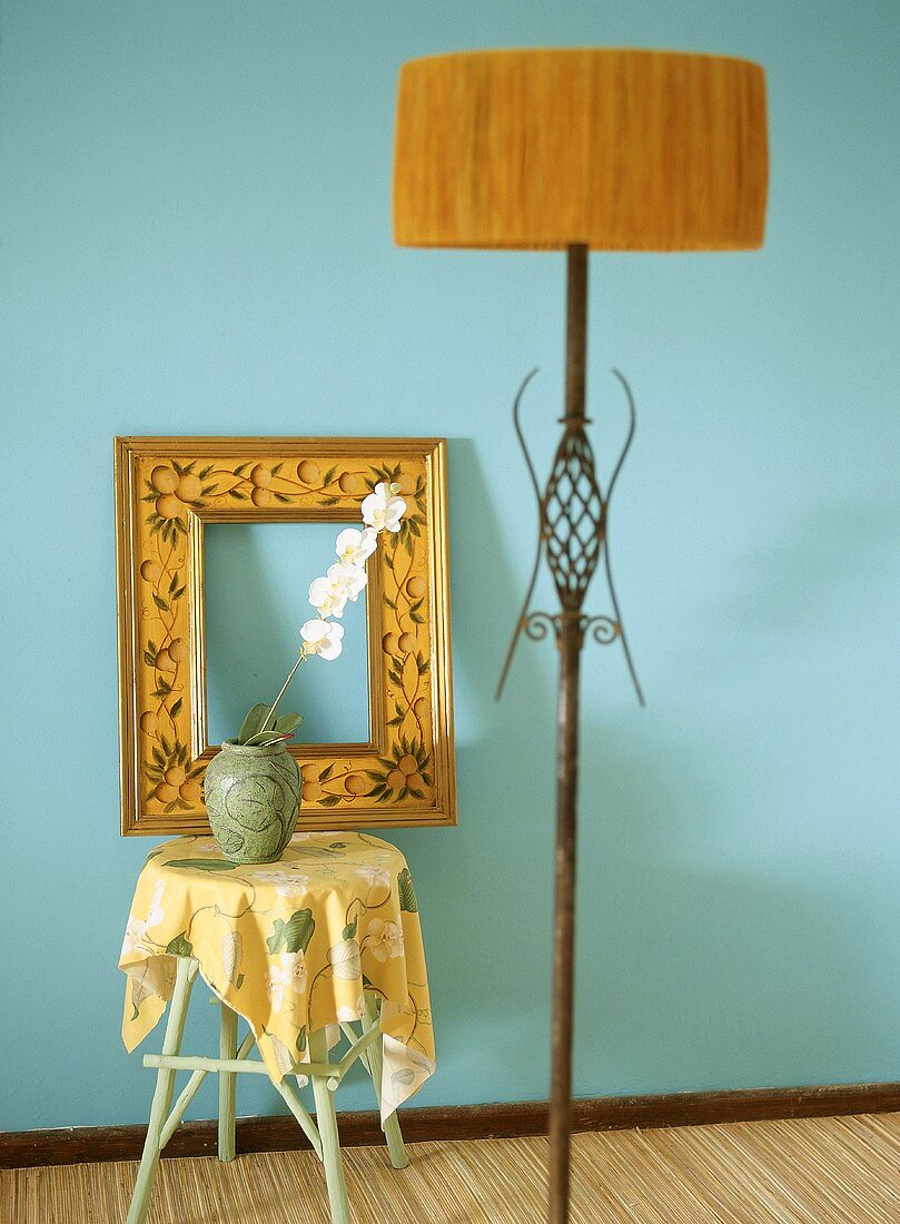 Stehlampe, Bilderrahmen und Orchidee in der Vase vor blaue Wand