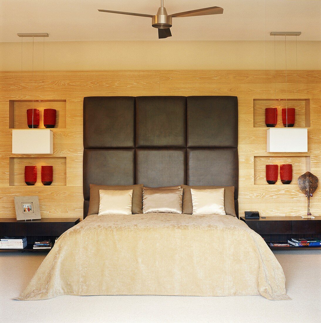 Schlafzimmer mit großem Doppelbett und Lederkopfteil vor Holzwand mit eingebauten Nischen