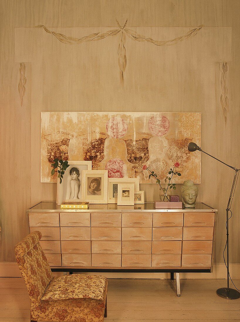 Holzkommode mit vielen Schubladen und Familienfotos vor rustikale Wand mit zeitgenössischem Gemälde