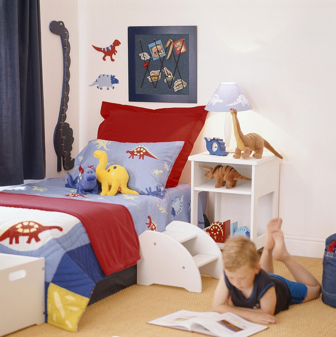 Junge liest ein Buch auf dem Boden seines Kinderzimmers mit Einzelbett und Kinderspielzeug