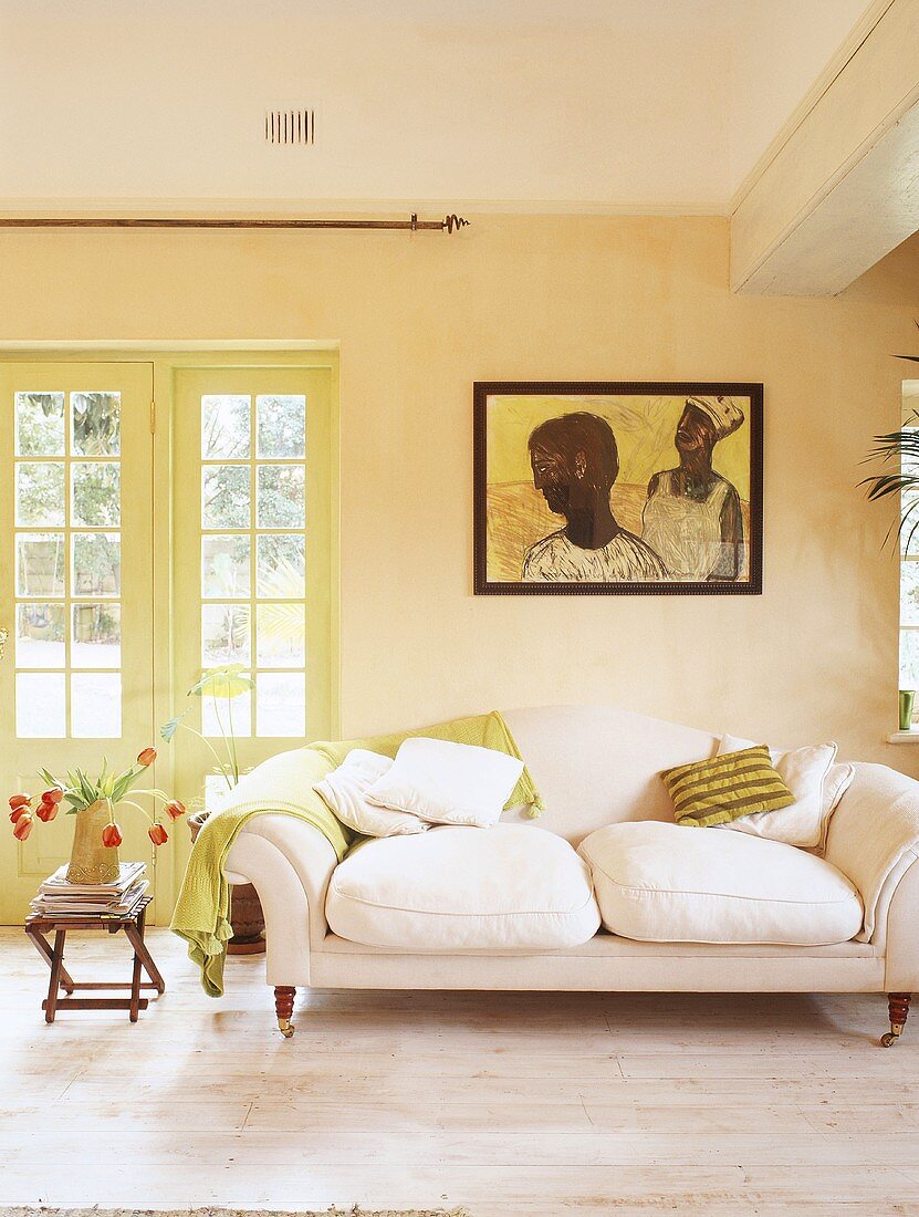 weiße 2-Sitzer Couch und mintgrüne Wolldecke unter Wandbild mit afrikanischem Motiv