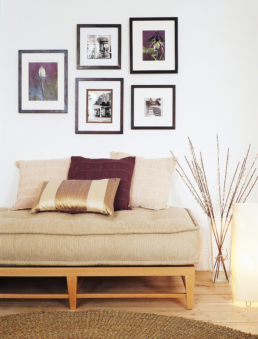 Niedrige Holzbank mit Sitzpolster und Kissen unter Bildersammlung an der Wand