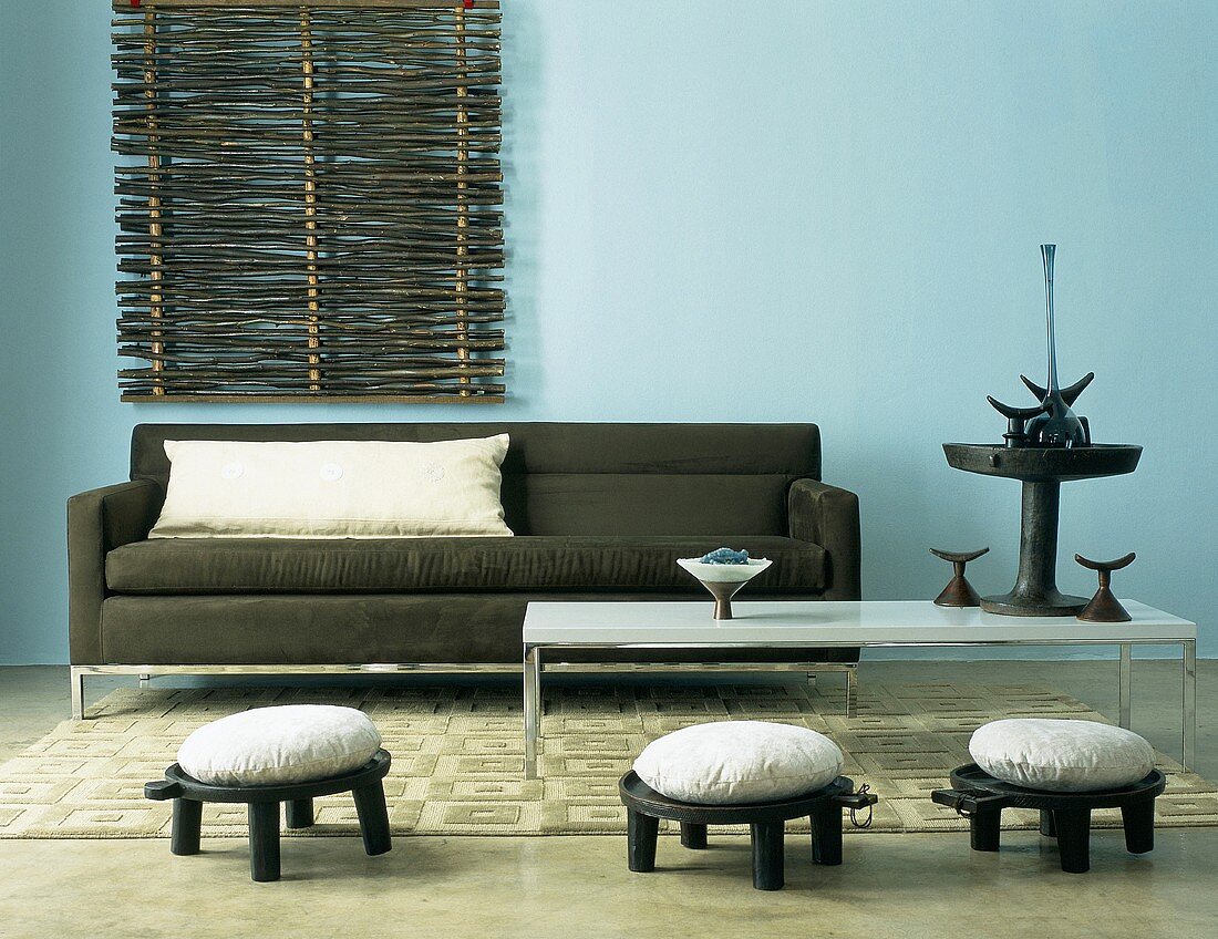 Dunkle Couch, weißer Couchtisch und kleine Hocker mit sitzkissen vor blaue Wand