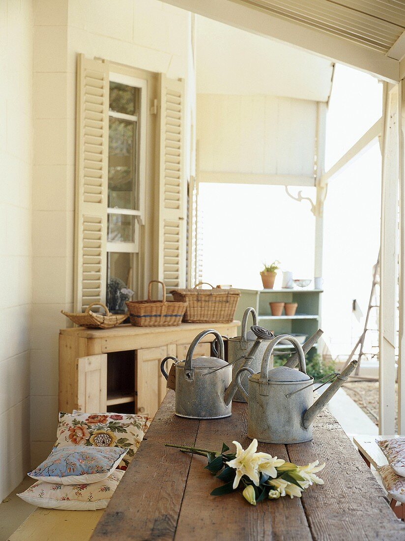 Ein rustikaler Holztisch mit Metallgießkannen und Lilienstrauß auf der Veranda