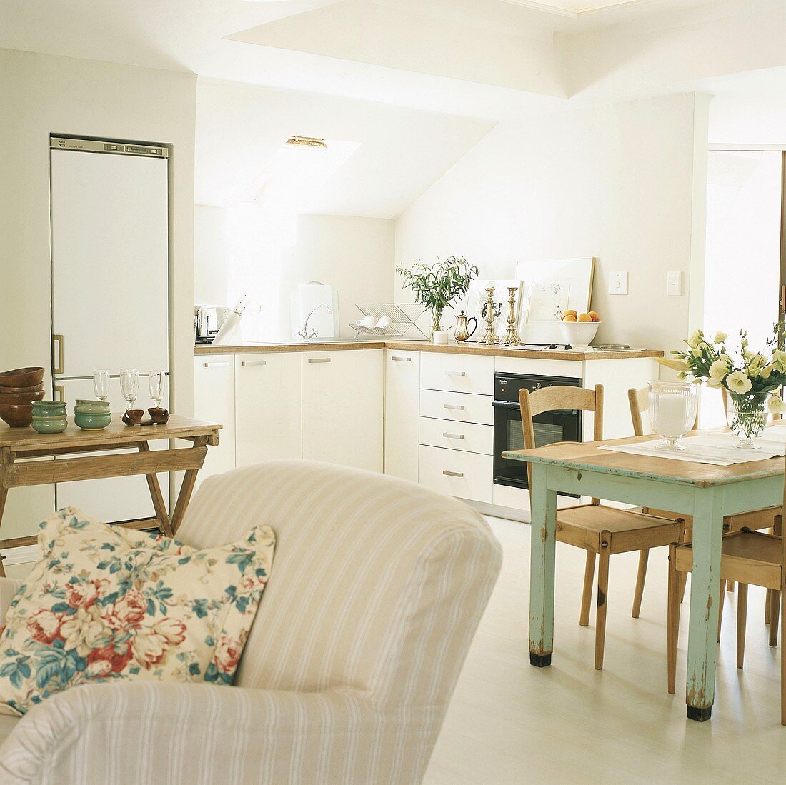 Kleine Küchenzeile unter Dachschrägen und eine Wandnische mit Kühlschrank im offenen Wohn- und Essraum