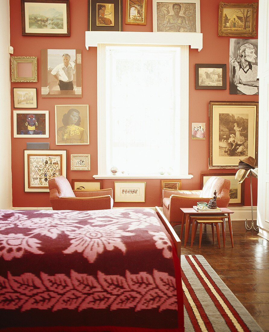 Eine dekorative Bildersammlung an der roten Wand eines Schlafzimmers