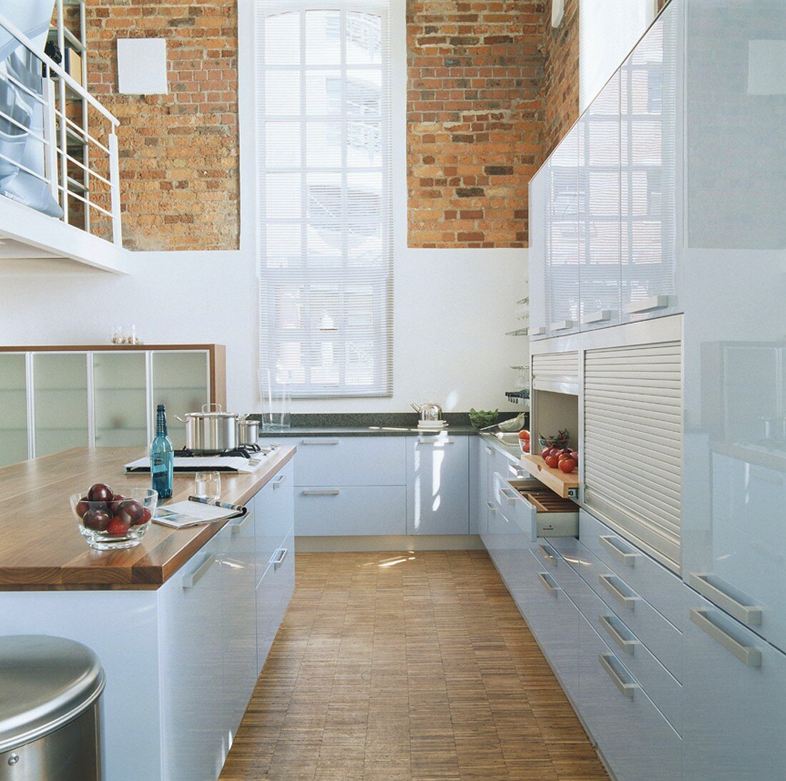Blick in eine hellblaue Hochglanzküche mit hohem Sprossenfenster und Backsteinwänden