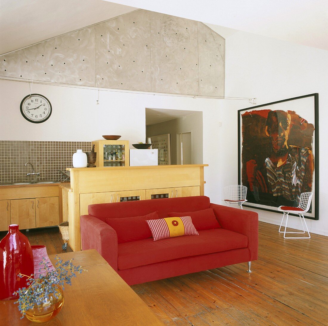 Rotes Sofa und großes, zeitgenössisches Gemälde in einem offenen Wohnraum mit Küchenzeile