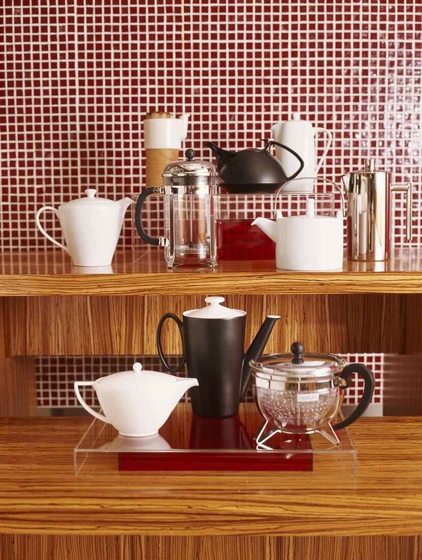 Various coffeepots and teapots on wooden surface in front of red mosaic wall tiles