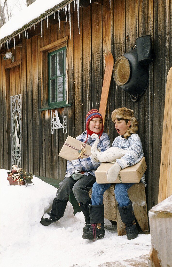 Two children sitting in front of wooden hut in winter