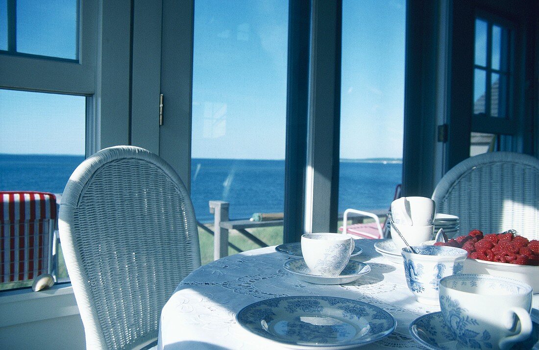 Tisch mit Tassen und Himbeeren, im Hintergrund das Meer