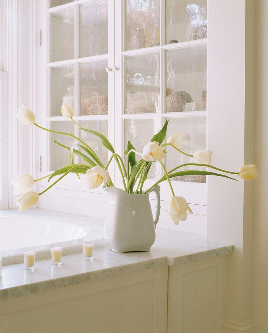 Weißer Tulpenstrauß auf Marmorplatte am Rand einer Badewanne